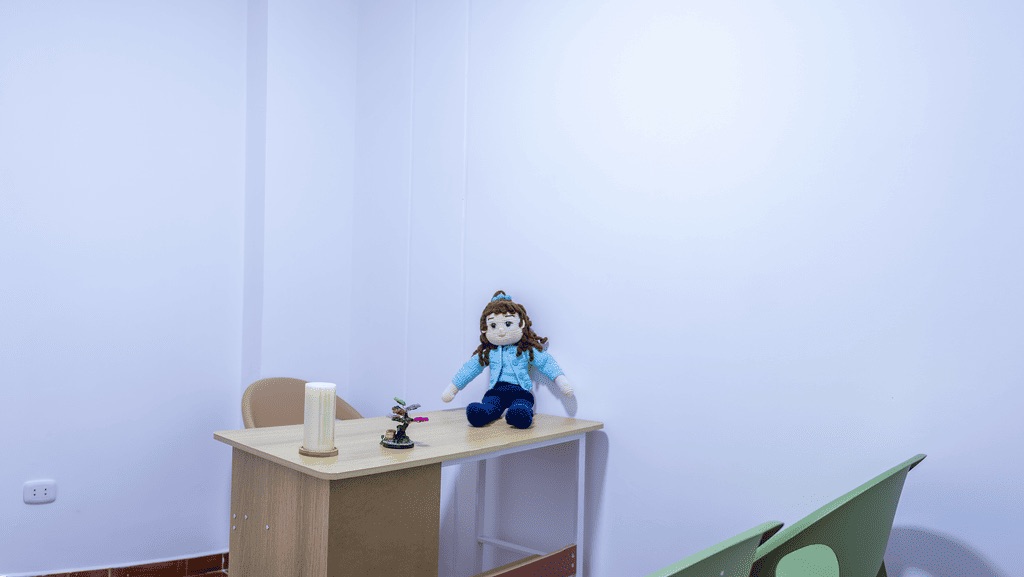 Consultorio de evaluación pediátrica con escritorio, sillas y muñeca terapéutica