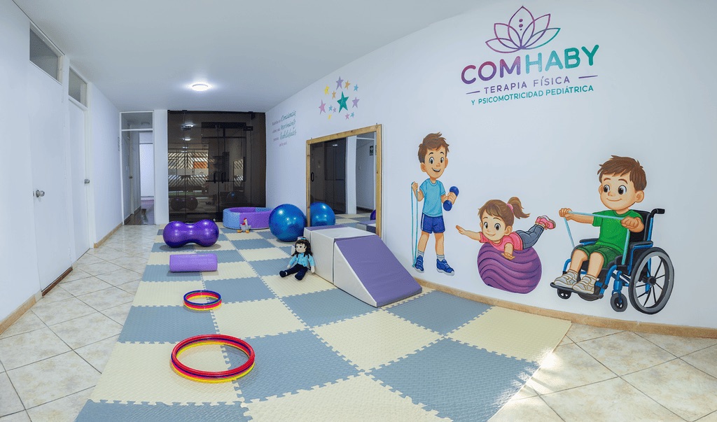Sala de terapia pediátrica COMHABY con material psicomotor, rampa, pelotas y mural infantil inclusivo