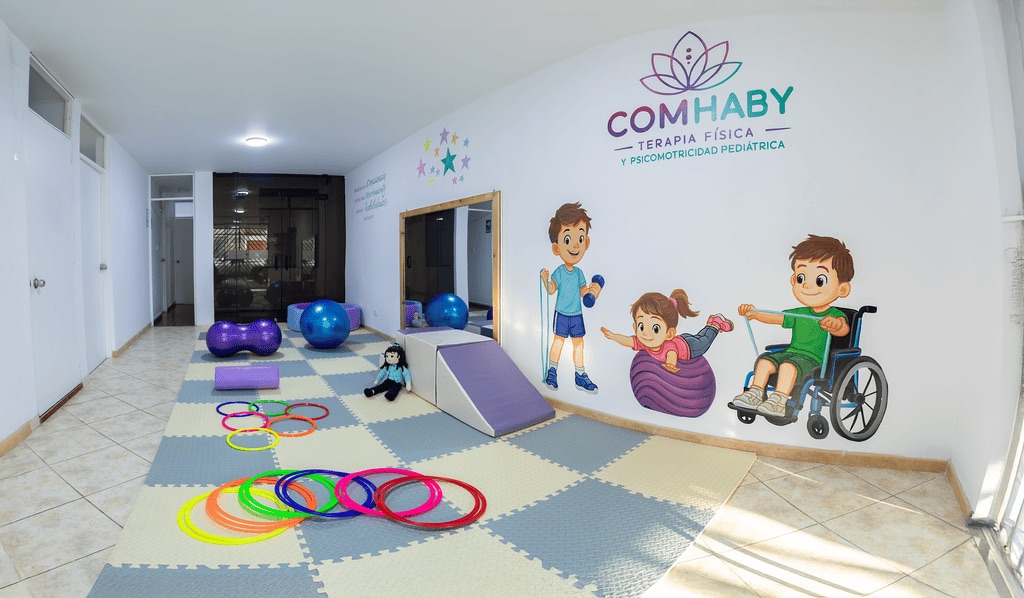 Sala de terapia física pediátrica de COMHABY con aros de colores, pelotas terapéuticas, espejo y rampa
